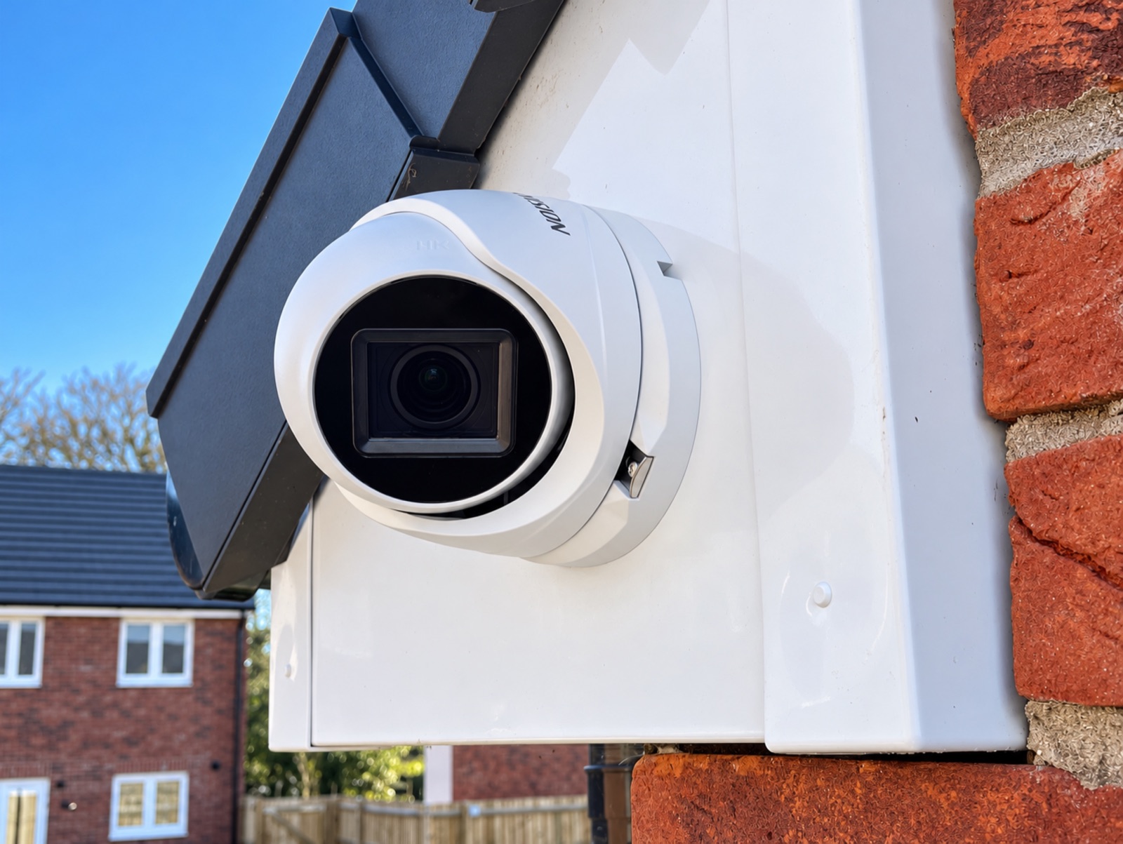 White CCTV turret camera mounted on the fascia beside a brick wall
